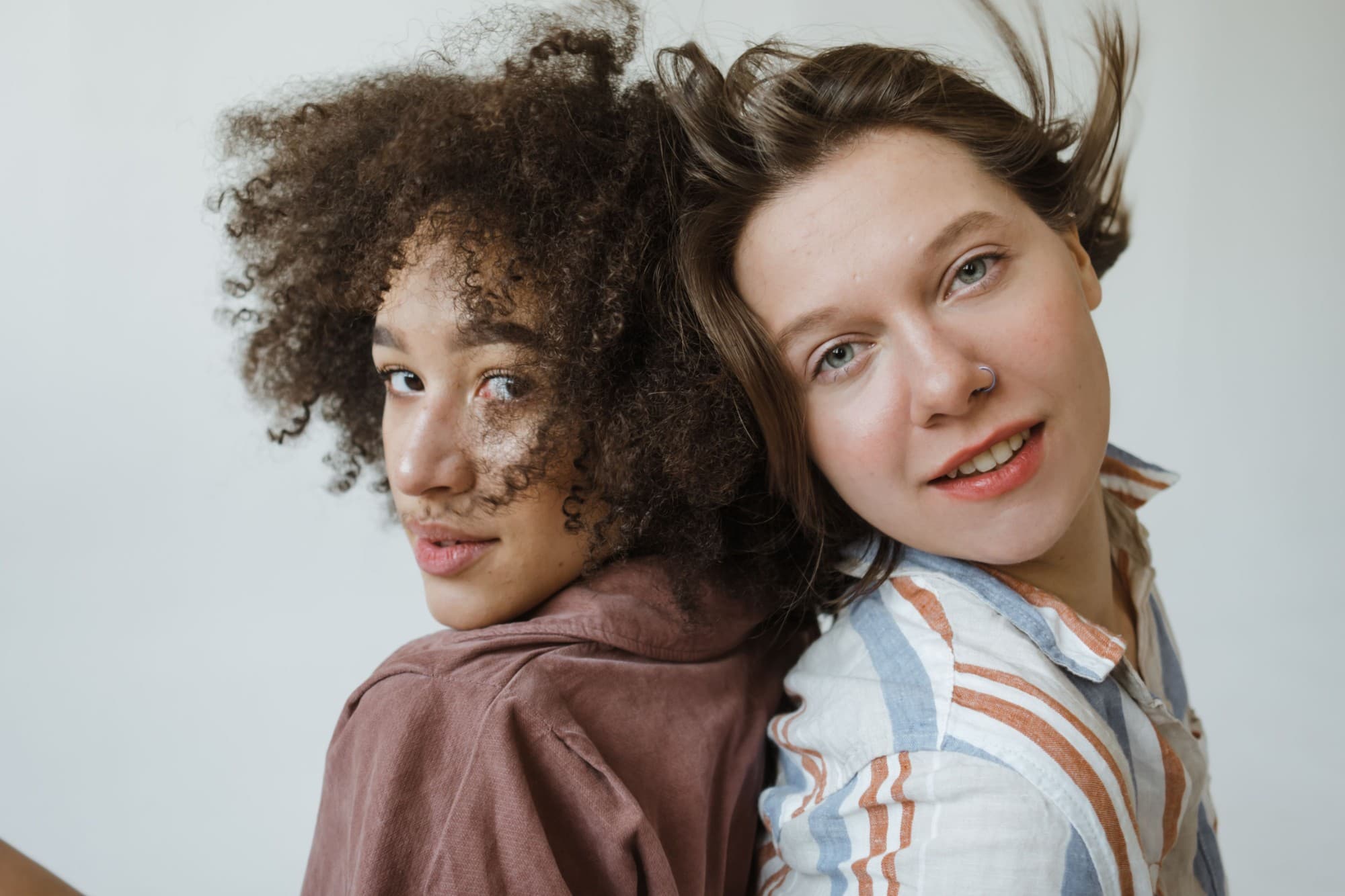 Two friends standing back to back, sharing a playful look at the camera